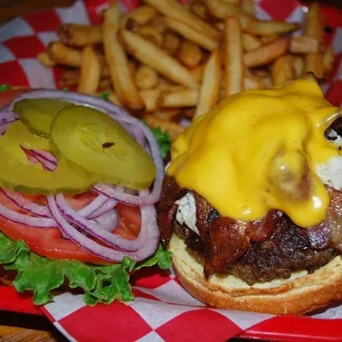 Open-faced burger with beef, bacon, cheese, fresh vegetables, and fries.
