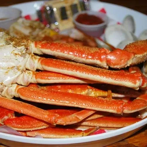 Piled high, orange-red cooked crab legs on a white plate.