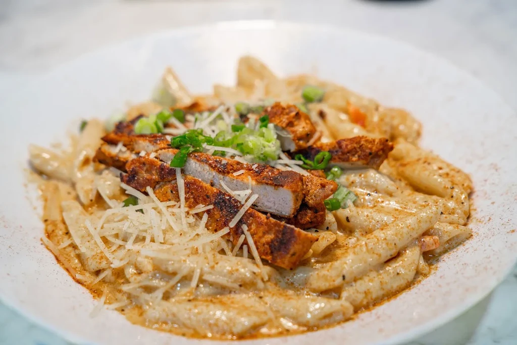 Dish of creamy pasta, grilled chicken, cheese, green onions, and spice.