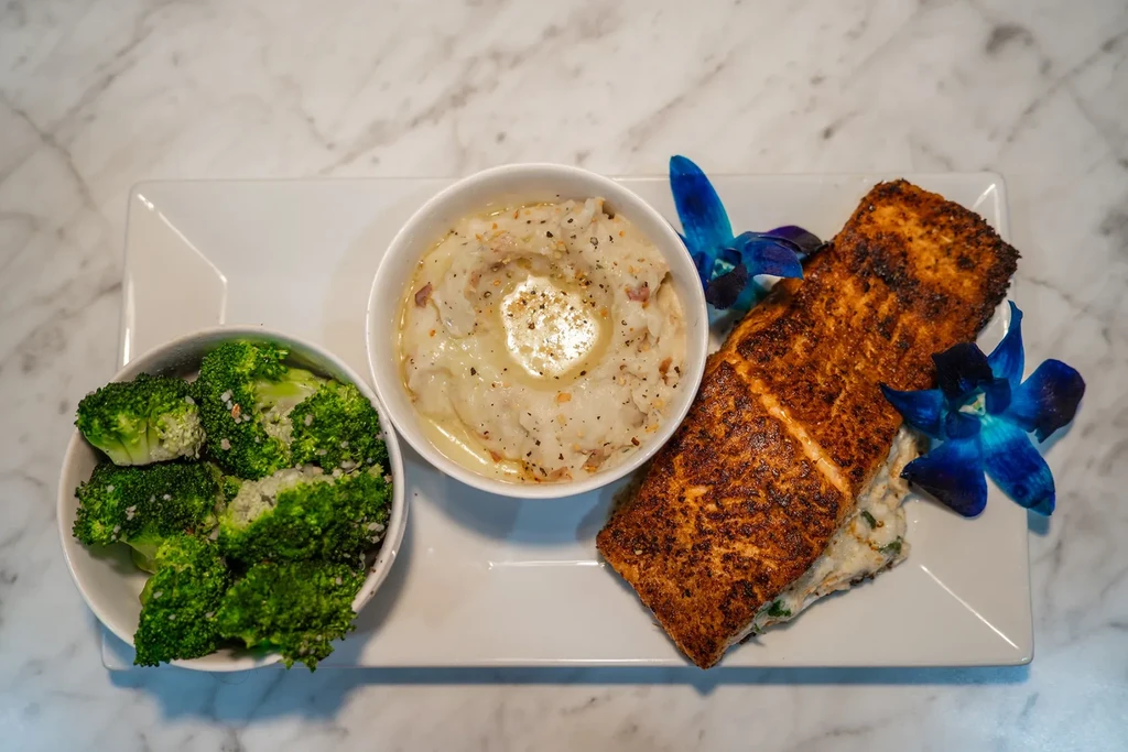 Seared salmon, mashed potatoes, broccoli, garnished with blue orchid flowers.