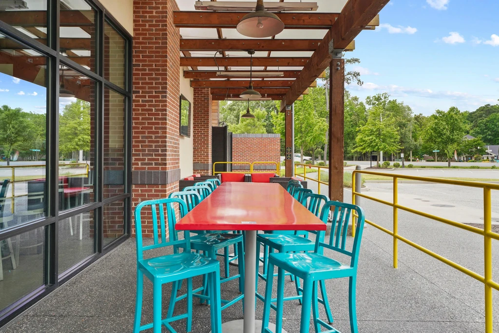 Outdoor restaurant patio with a red table, teal stools, and a pergola.