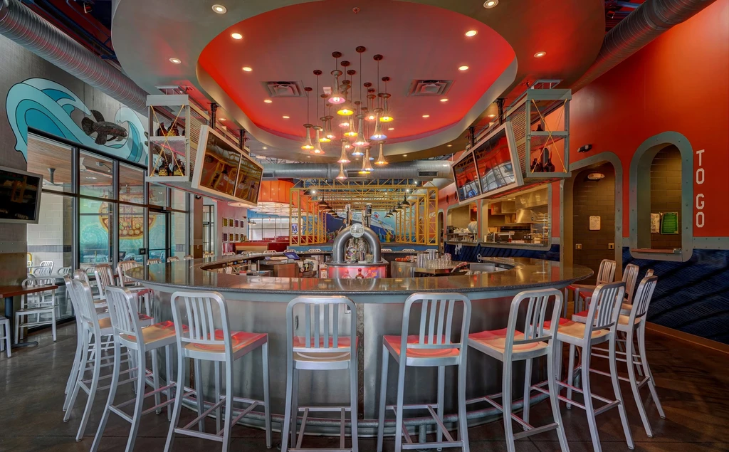 Empty modern restaurant bar with metallic counter, red seats, and murals.