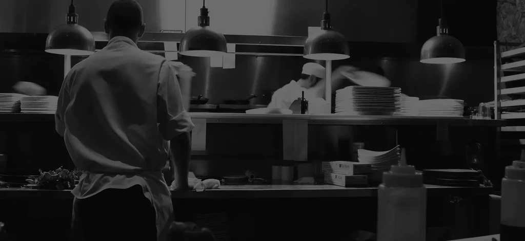 A busy professional kitchen with two chefs, one blurred from motion.