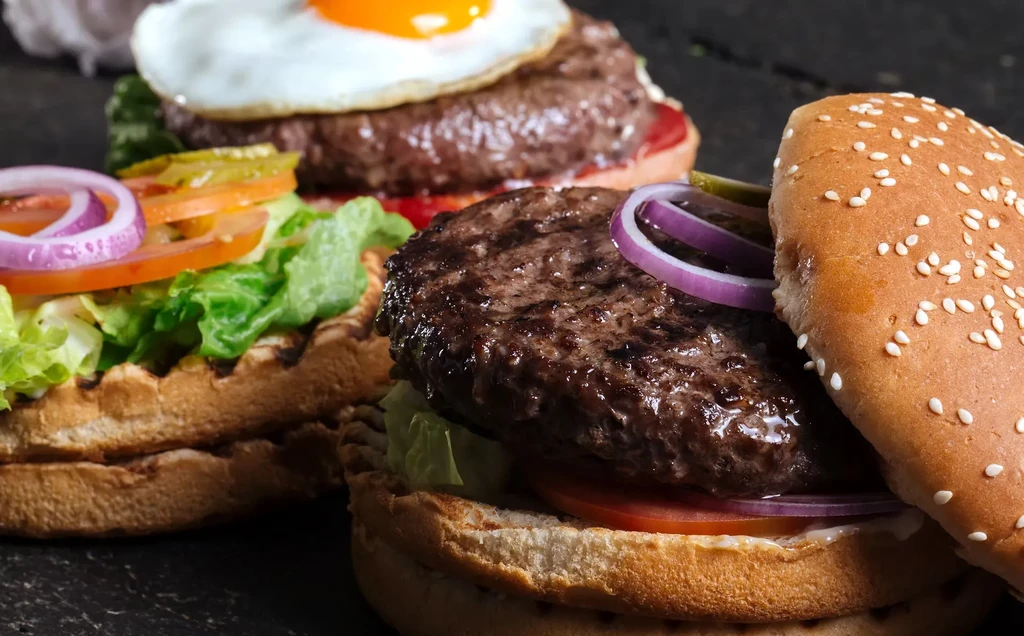 Close-up of two gourmet burgers; one reveals beef patty, one has egg.