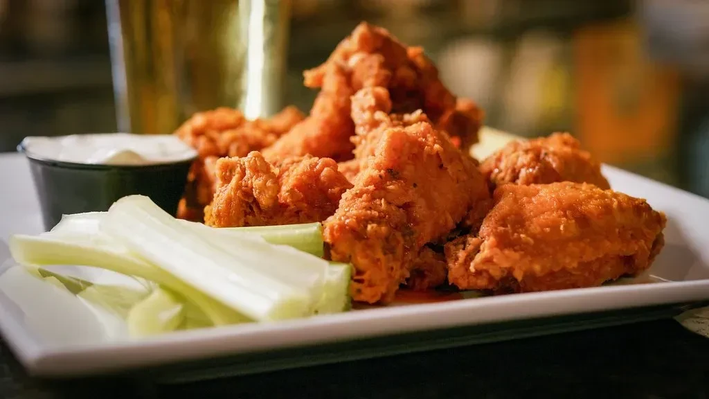 Crispy chicken wings with celery and creamy dip on a white plate.