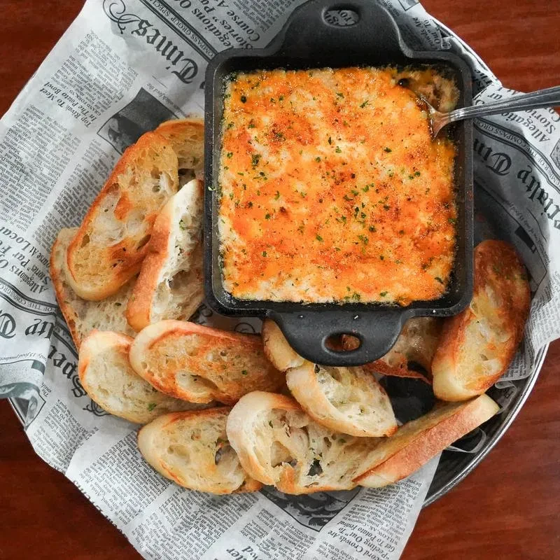 Bubbling dip with herbs in skillet, surrounded by toasted baguette slices.