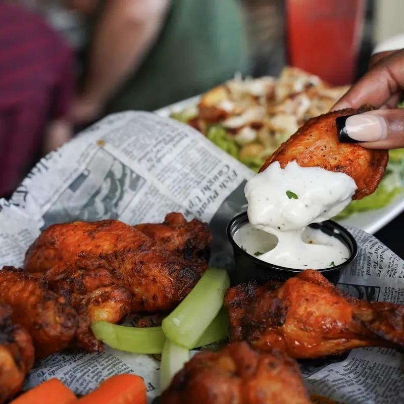 Hand dipping a crispy chicken wing into creamy white sauce.
