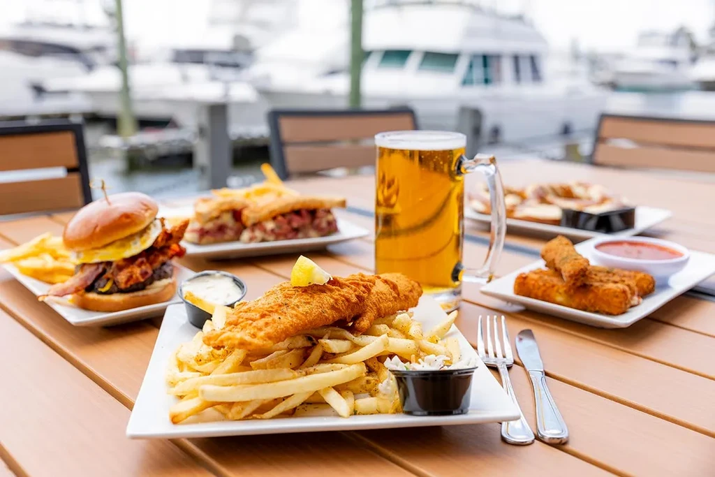 Waterfront table set with fish, chips, burger, beer, and mozzarella sticks.