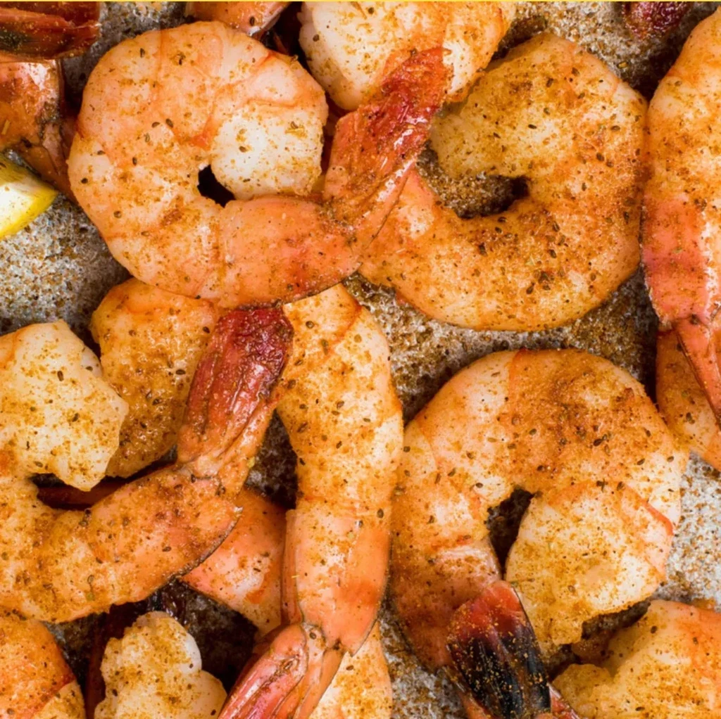 Heavily seasoned pinkish-orange cooked shrimp with a lemon wedge.