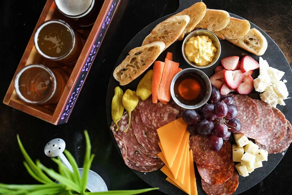 Charcuterie board with meats, cheeses, fruits, and a three-glass beer flight.
