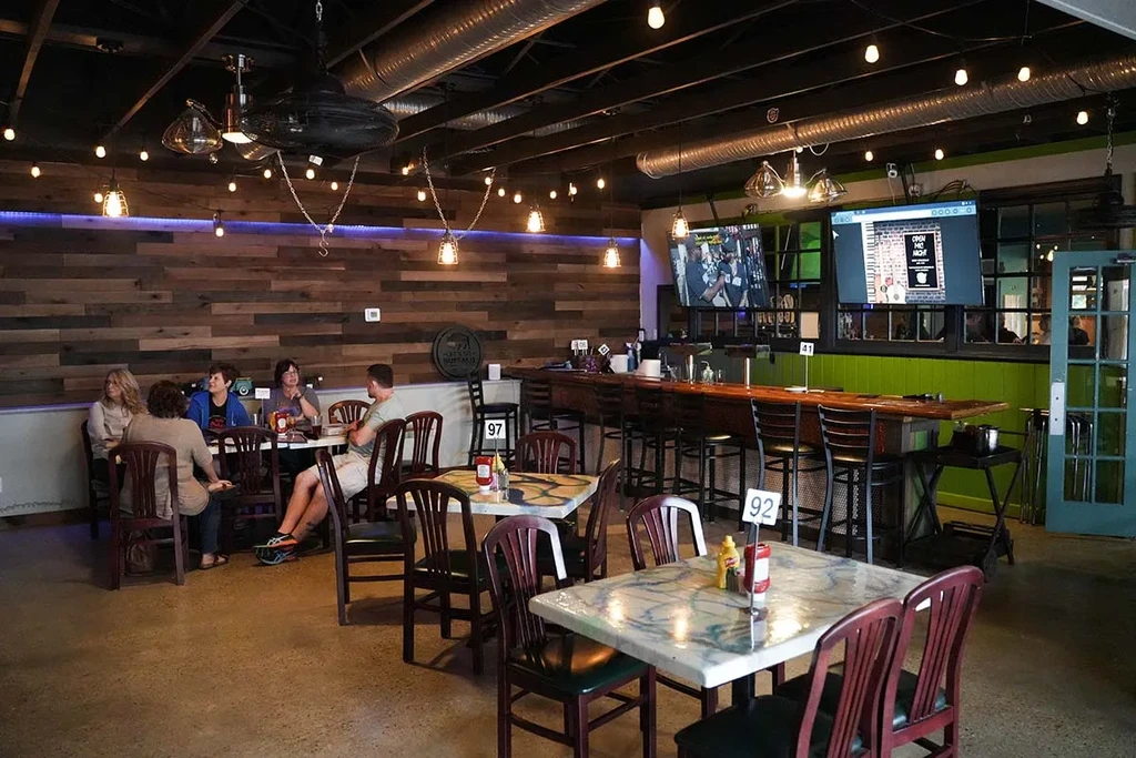 Modern industrial-chic restaurant interior with bar, tables, and flat-screen TVs.