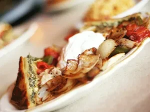 Savory quiche, sautéed vegetables, and cream on a white wavy plate.