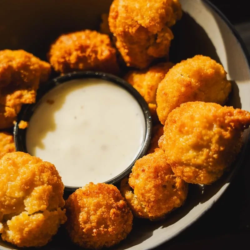 Golden-brown fried items piled in a bowl with white dipping sauce.