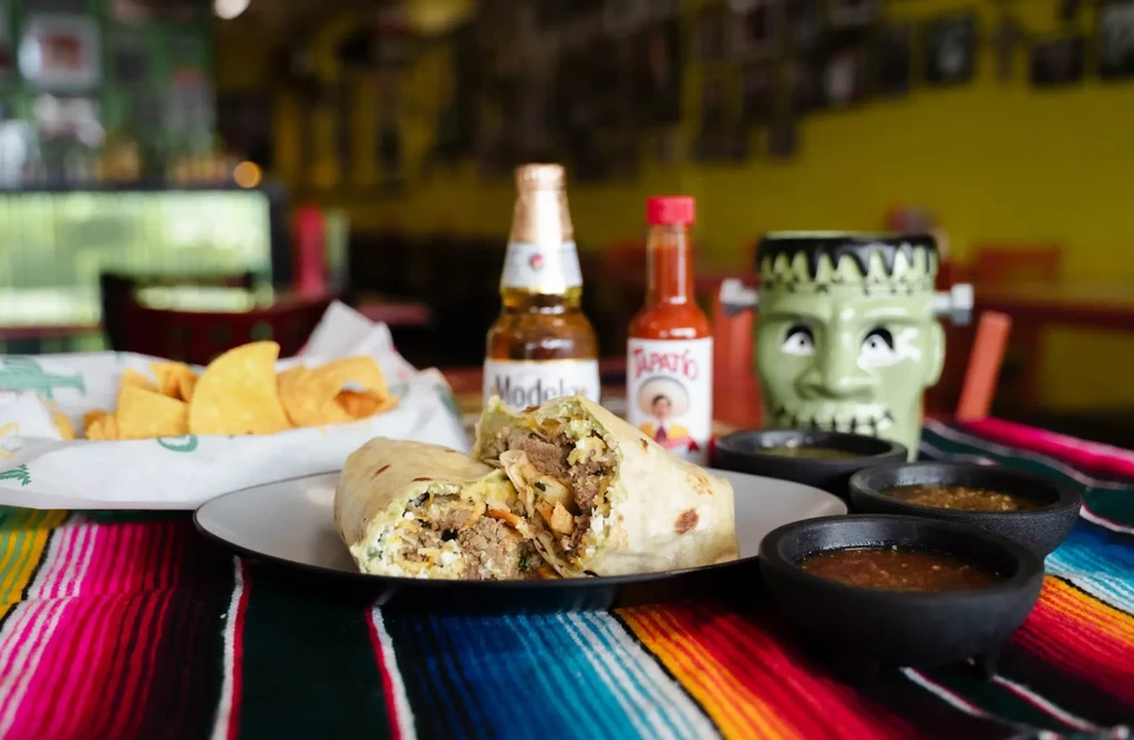Vibrant Mexican restaurant meal: cut burrito, salsas, chips, and beer.