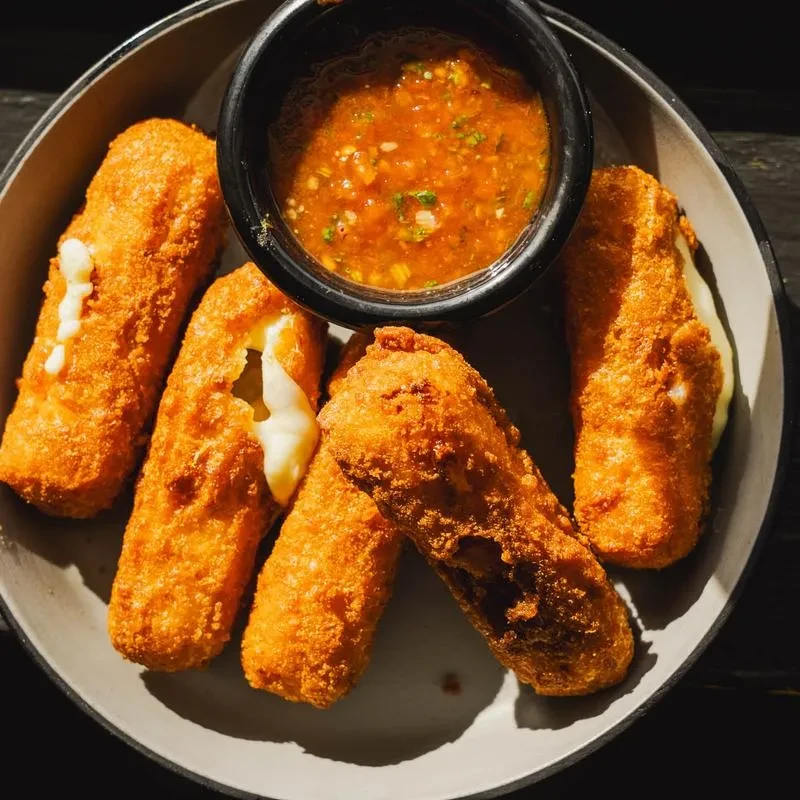 Five golden-brown mozzarella sticks with melted, stretching cheese and marinara sauce.