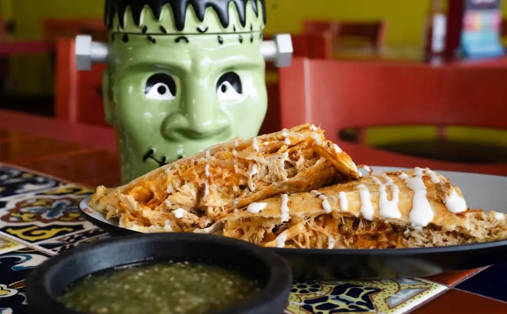 Two stuffed pastries with shredded meat, creamy sauce, green salsa, Frankenstein mug.