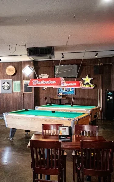 Bar interior featuring two pool tables under Budweiser signs.