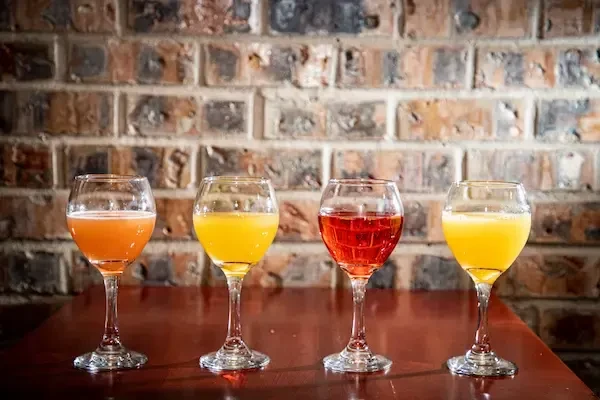 Four stemmed glasses with colorful drinks against a brick wall.