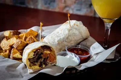 Two burritos, cut open, served with home fries and dipping sauces.
