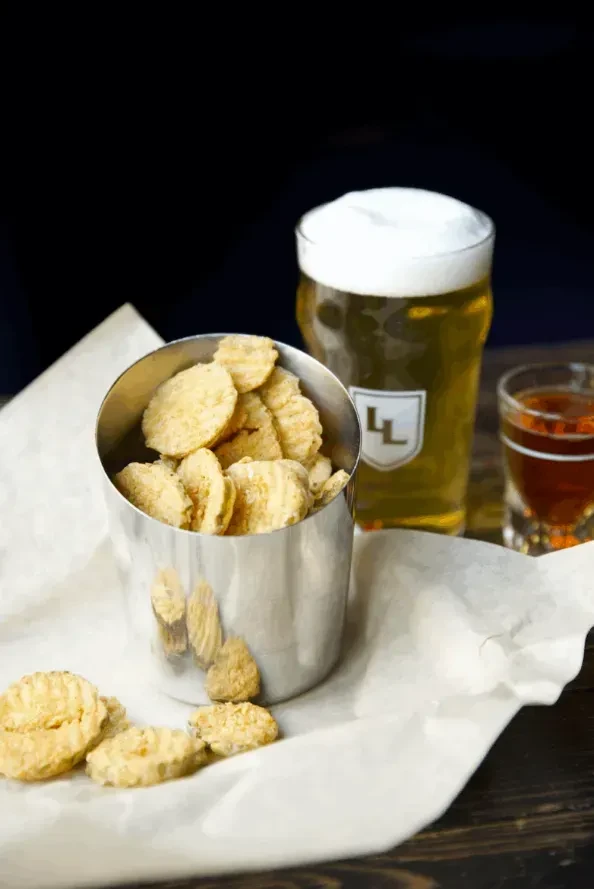 Overflowing fried pickle chips, beer pint, and a shot glass.