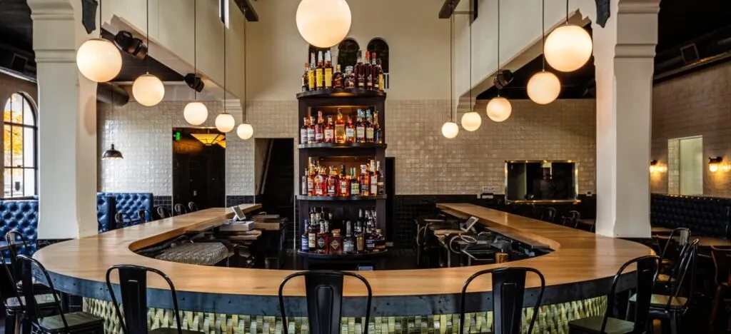 Stylish bar interior with U-shaped counter, stocked liquor shelf, no people.