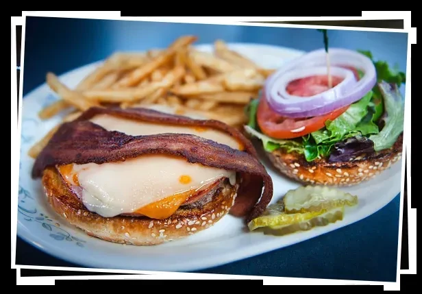 An open-faced burger with cheese, bacon, lettuce, fries, and pickles.