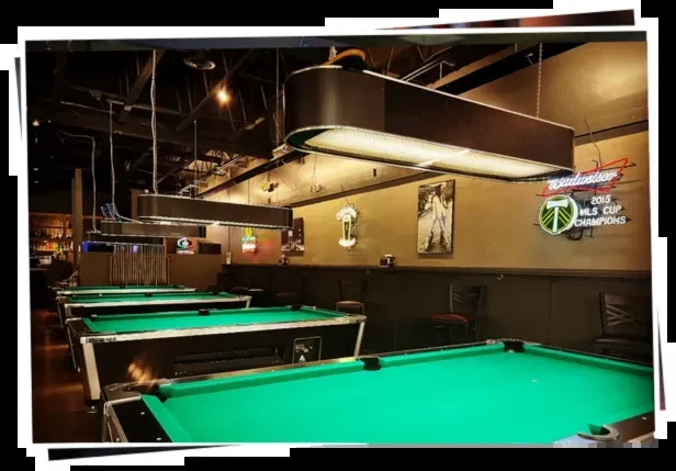Empty, dimly lit pool hall with green tables and MLS Cup sign.