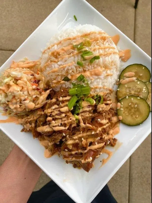 A plate of rice, pulled meat, coleslaw, and cucumber with sauce.
