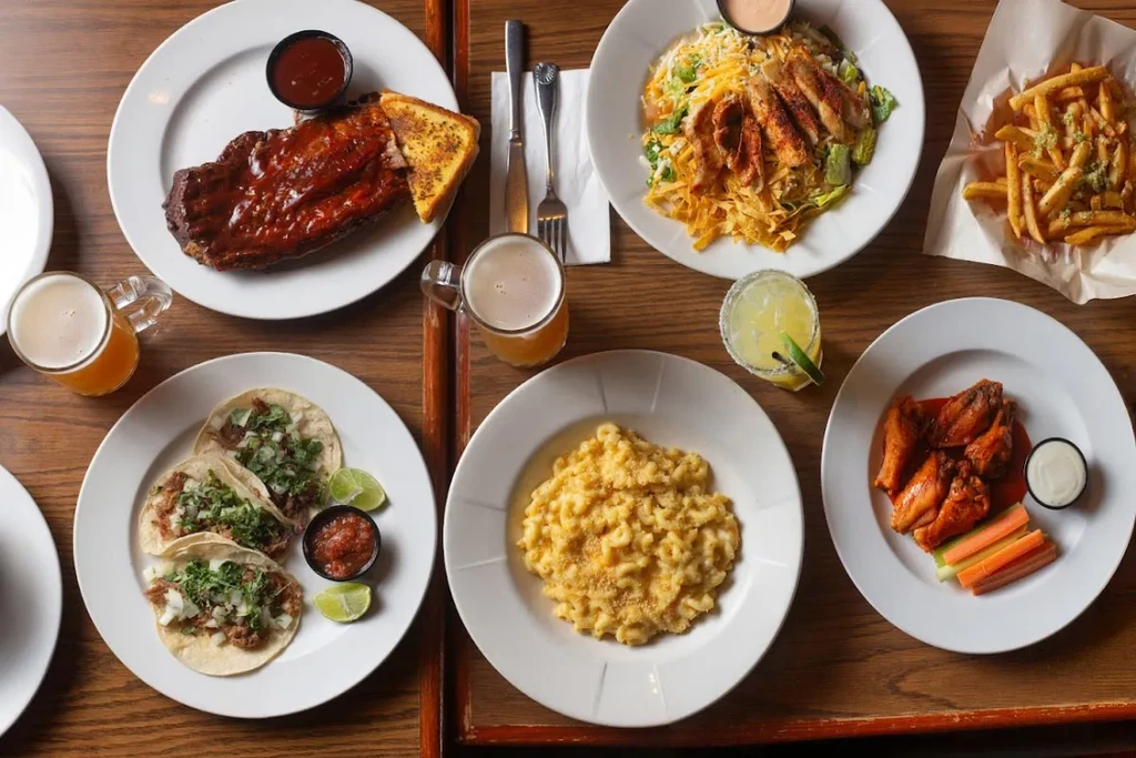 Diverse comfort food spread: ribs, tacos, wings, salad, mac and cheese, drinks.