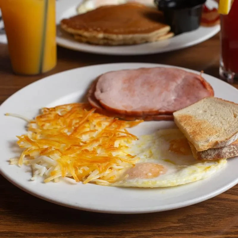 Breakfast plate with hash browns, fried eggs, ham, and toast.