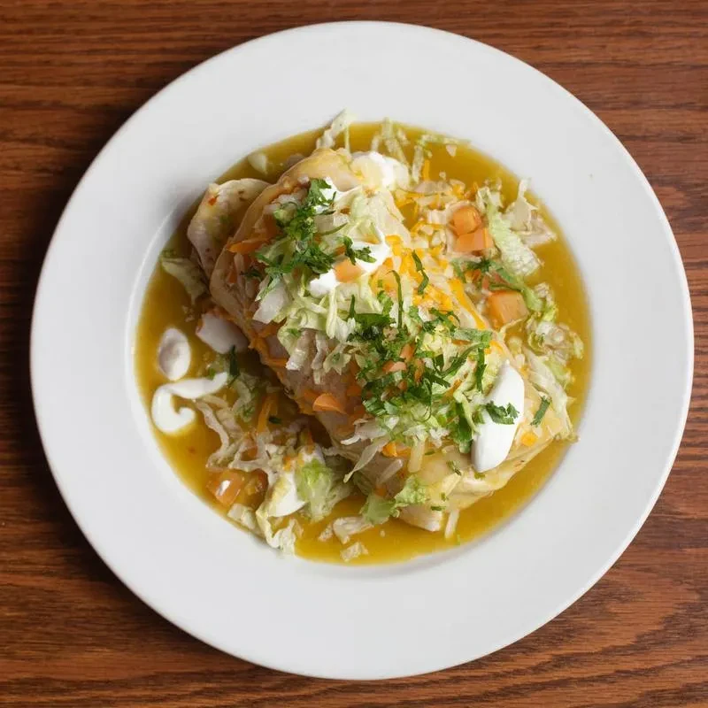Overhead: Enchilada-style dish with yellow-green sauce, lettuce, cheese, and crema.