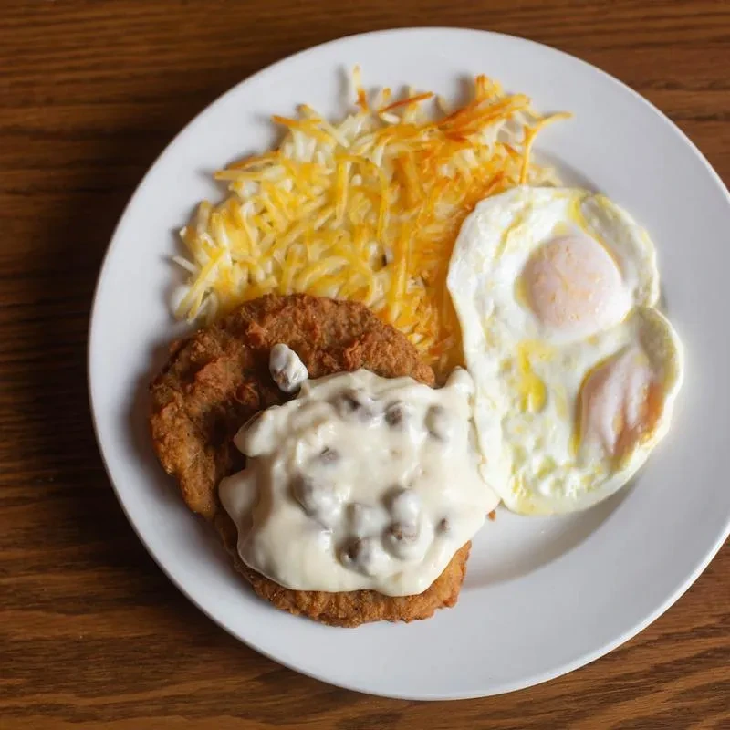 Breakfast plate: hash brown, two sunny-side eggs, gravy on a breaded patty.