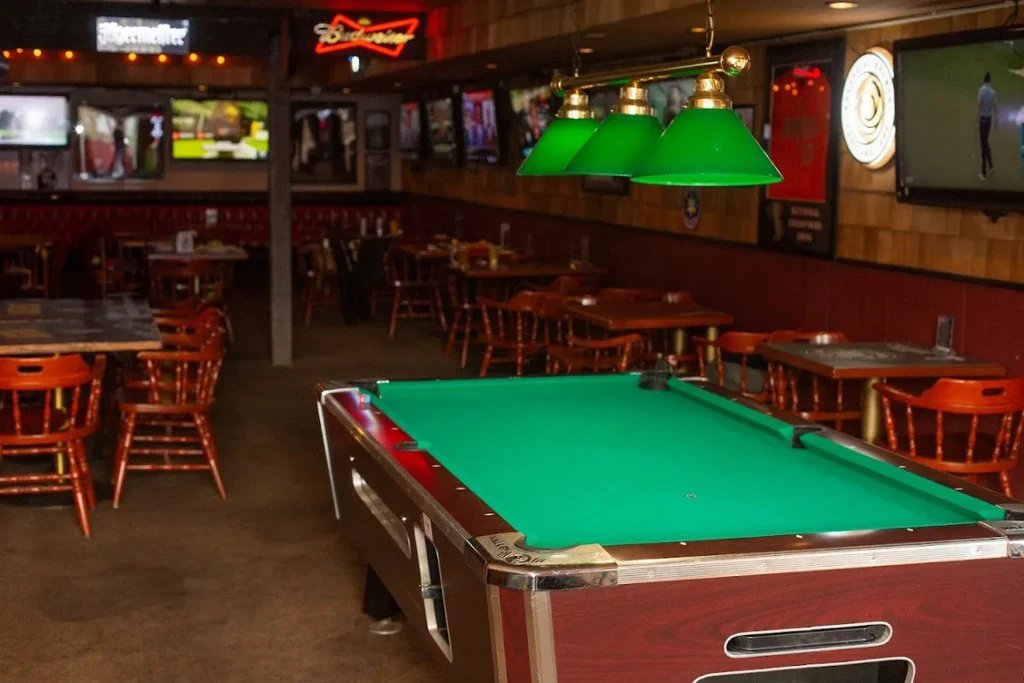 Dimly lit bar interior with pool table, TVs, and neon signs.