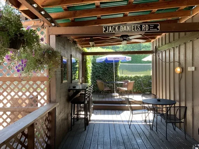 Rustic wooden outdoor patio with plants, tables, and Jack Daniel's sign.