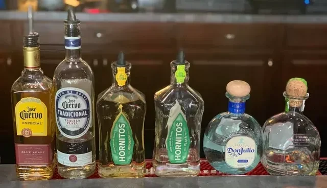 Six tequila bottles with pour spouts on a bar counter.