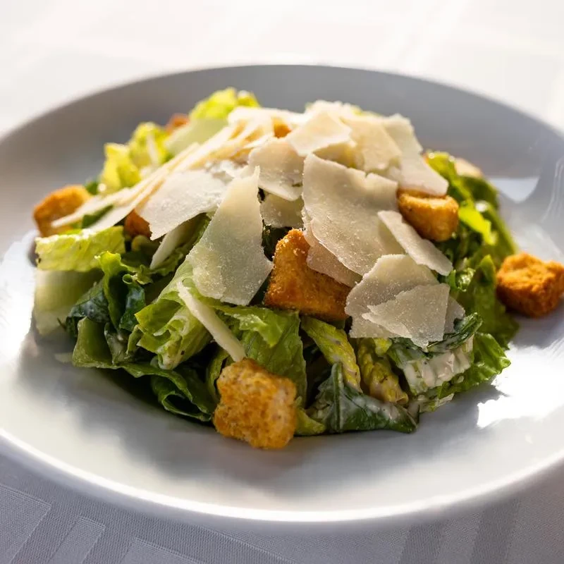 Caesar salad on white plate: romaine, croutons, Parmesan, creamy dressing.