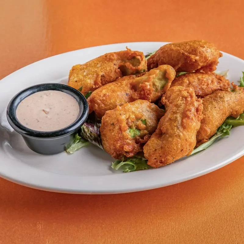 Plate of fried jalapeno poppers, dipping sauce, lettuce, orange background.