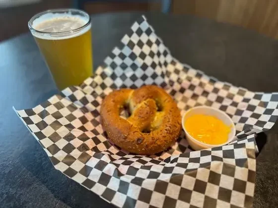Golden pretzel, cheese dip, and amber beer on checkered paper.