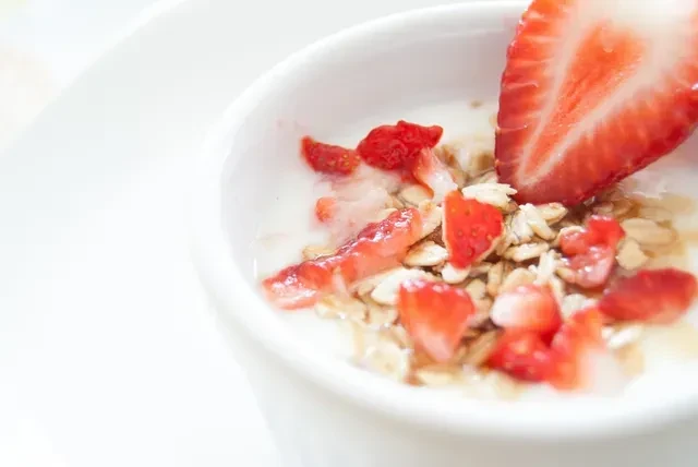 White bowl of yogurt topped with strawberries and granola.