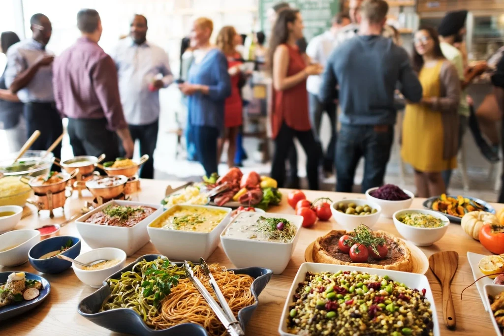 A diverse, colorful buffet with pasta, salads, and hot dishes; blurred people.