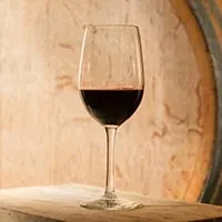 Clear glass of red wine on wood, barrel in background.