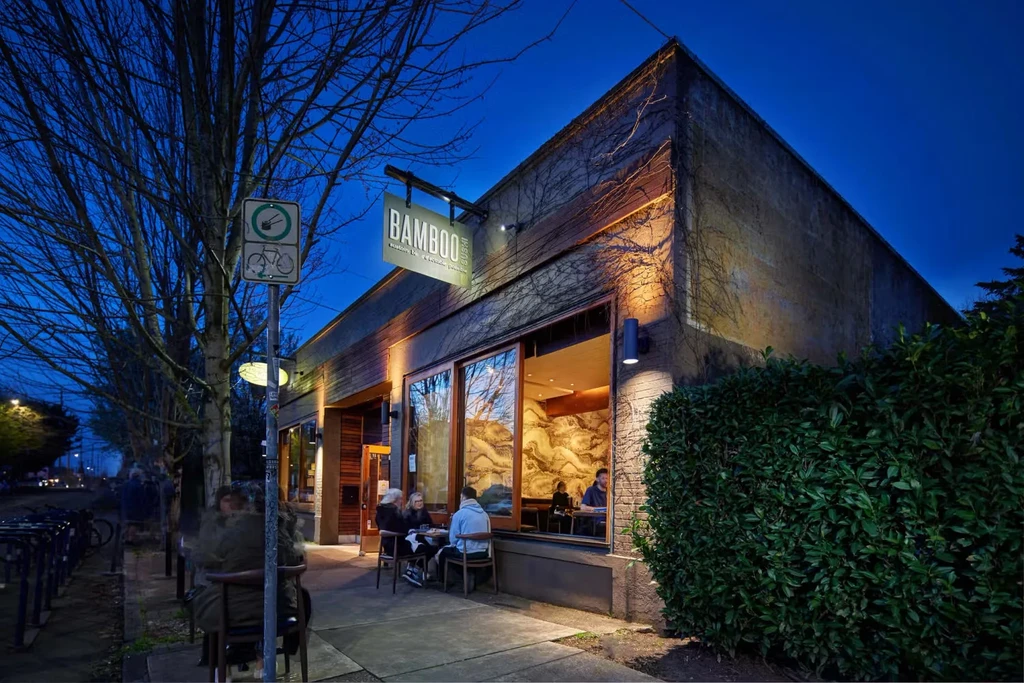 Modern BAMBOO Sushi restaurant exterior at dusk, people on patio.