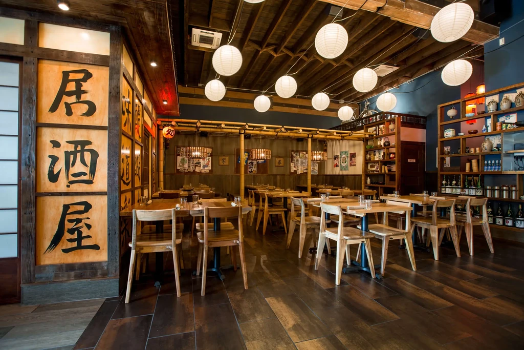 Japanese restaurant interior with empty tables, calligraphy, lanterns, and shelving.