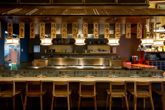 Warmly lit traditional Japanese restaurant with counter seating and menu signs.