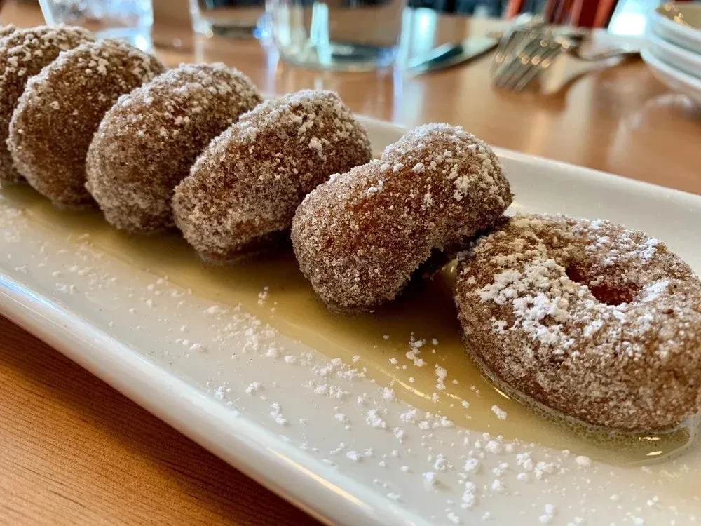 Five powdered sugar-dusted fritters in golden syrup on a white plate.