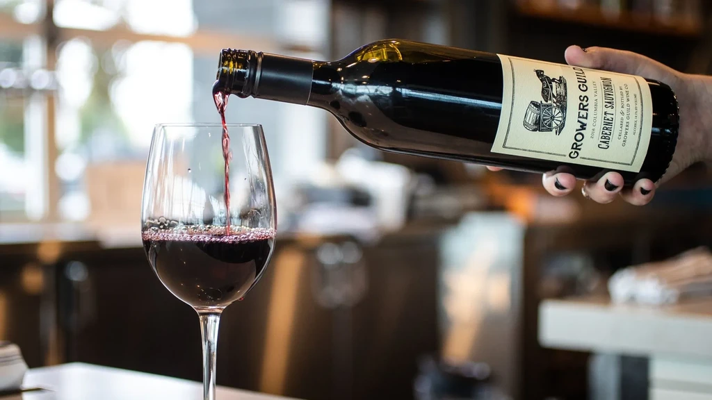 Close-up: Hand pours red wine from bottle into glass.