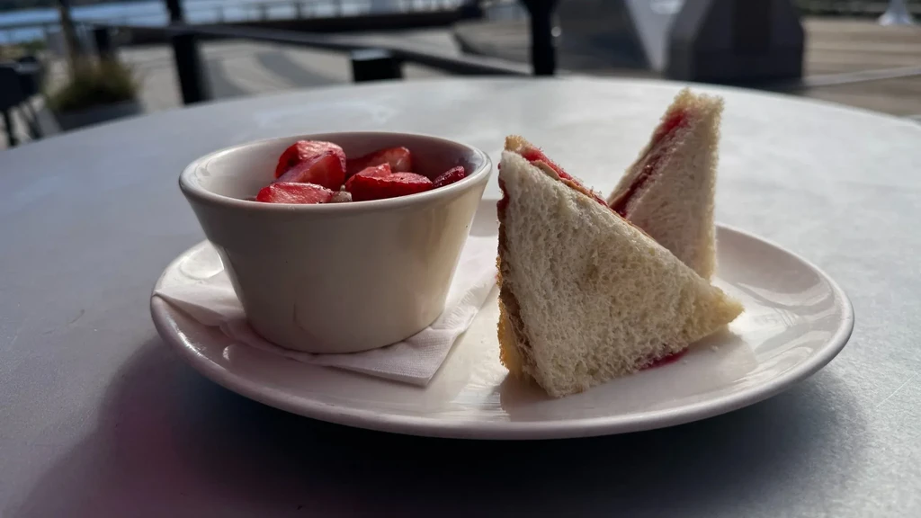 Triangular sandwich and sliced strawberries on an outdoor table by water.