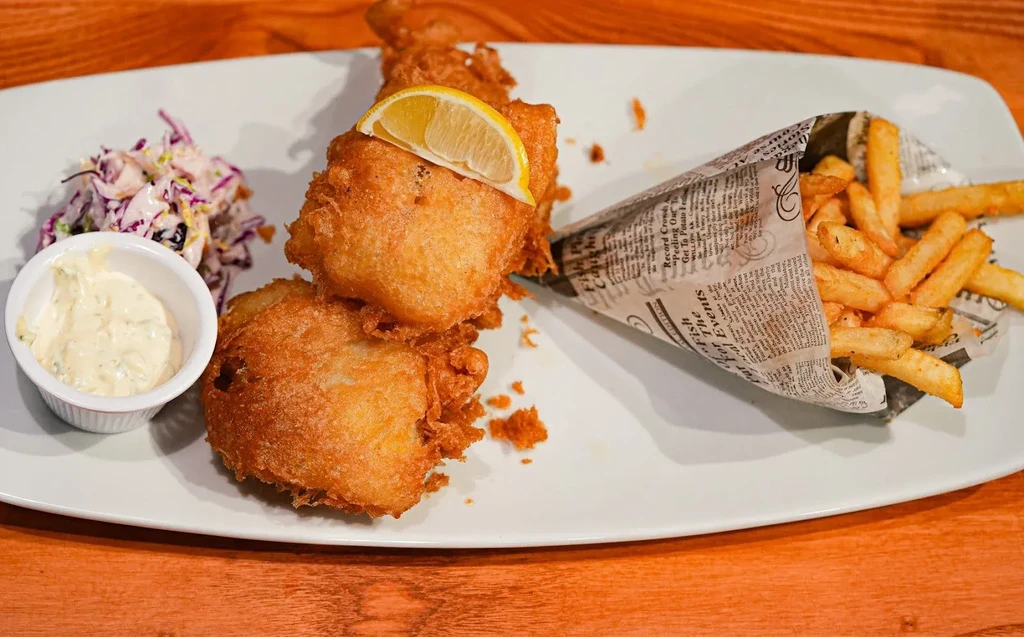 Battered fish, french fries, lemon, tartar sauce, and coleslaw.