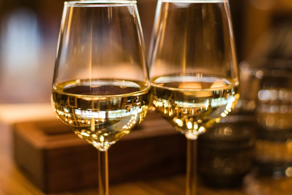 Two elegant wine glasses filled with white wine against blurred bokeh lights.