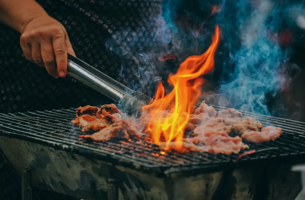 Close-up of meat being turned with tongs over hot grill flames.